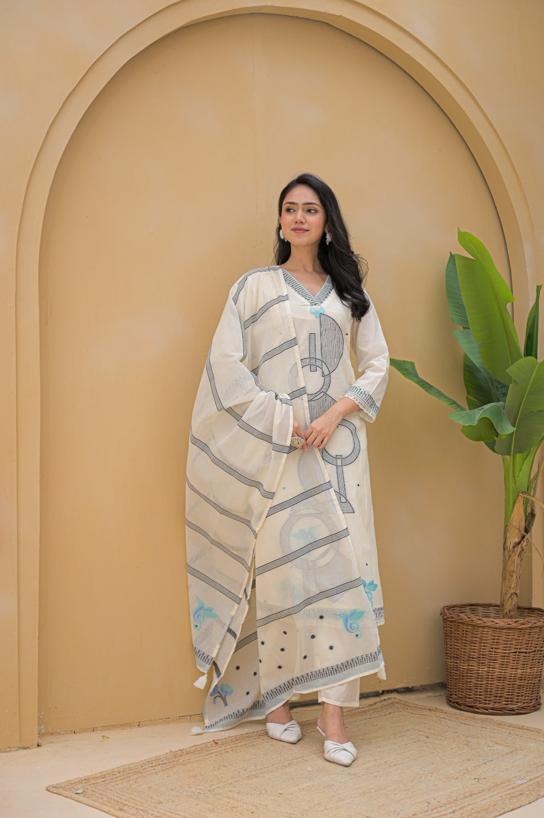 Woman wearing a cream embroidered suit set with blue floral details standing by an archway