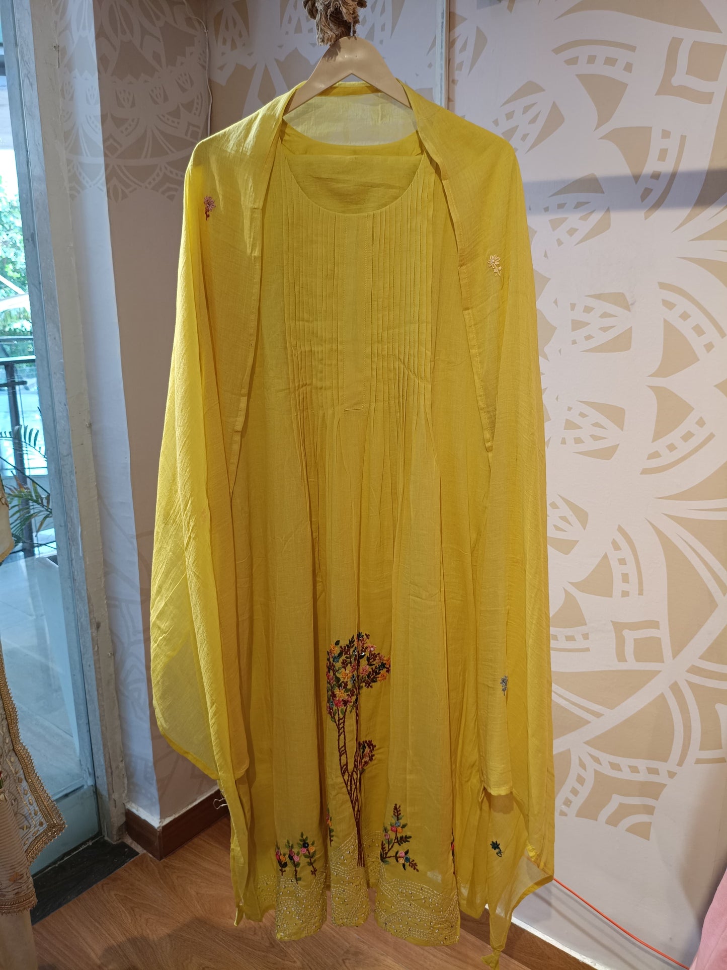 Yellow embroidered cotton dress with floral embroidery and matching dupatta hanging on wooden hanger