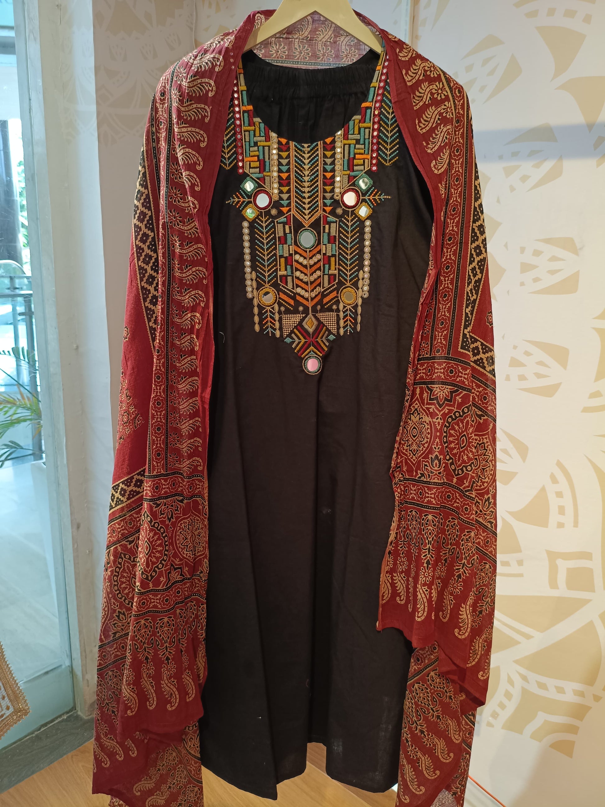 Black cotton festive suit with colorful embroidered neckline and red patterned shawl from Dharini's Store