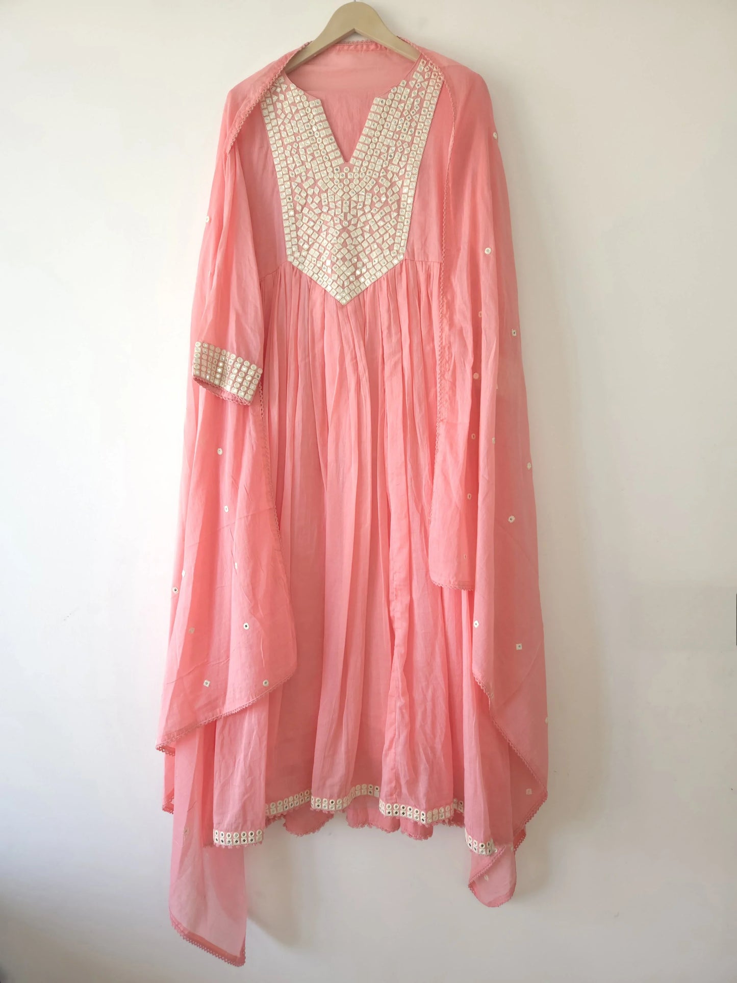 Pink cotton anarkali dress for women with white embroidery and matching dupatta hanging on wooden hanger