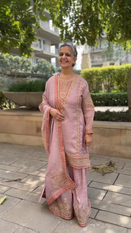 Elegant woman wearing a pink festive garara set for women with intricate embroidery outdoors