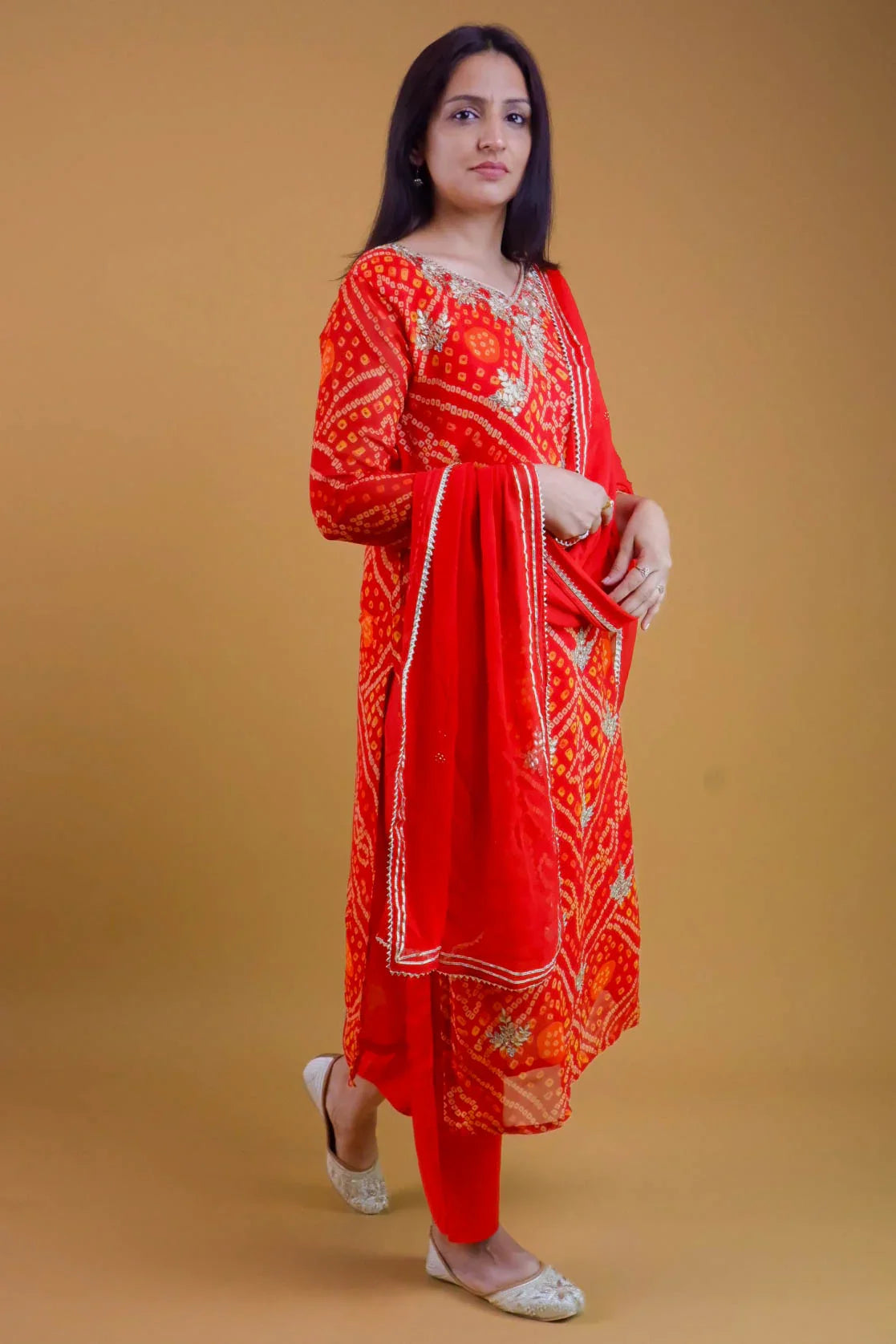 Woman wearing a red Georgette Bandhani suit online with matching dupatta and white flats