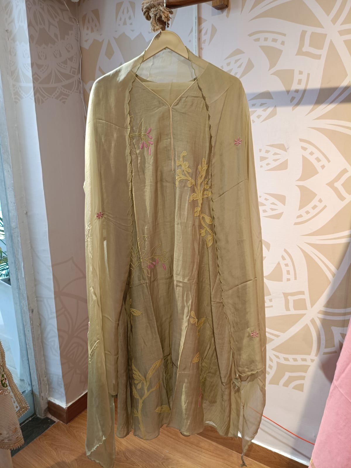 Olive chanderi embroidered suit hanging on wooden hanger showcasing delicate floral embroidery