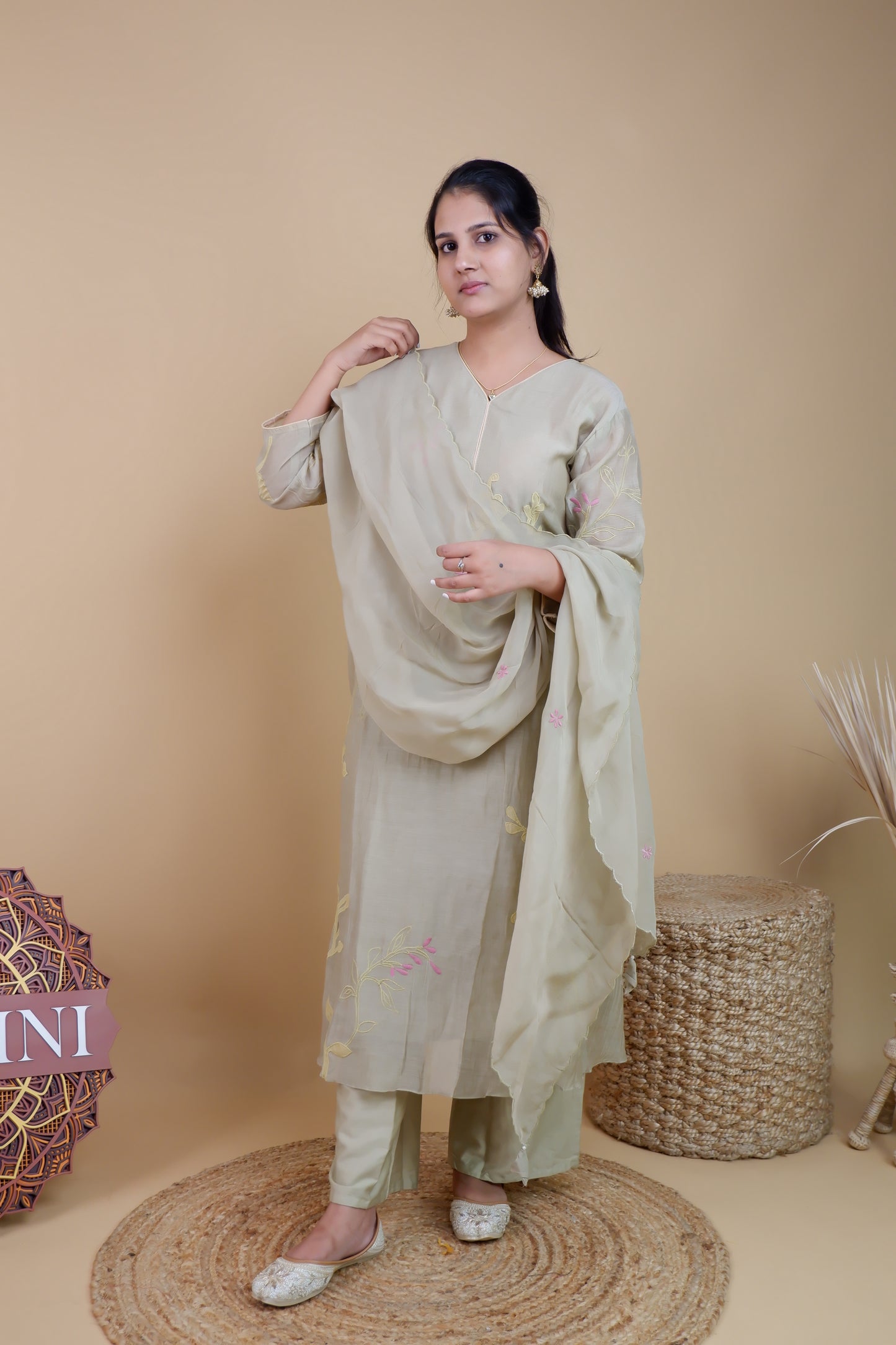 Woman wearing olive chanderi embroidered suit with matching dupatta and pants standing against beige background