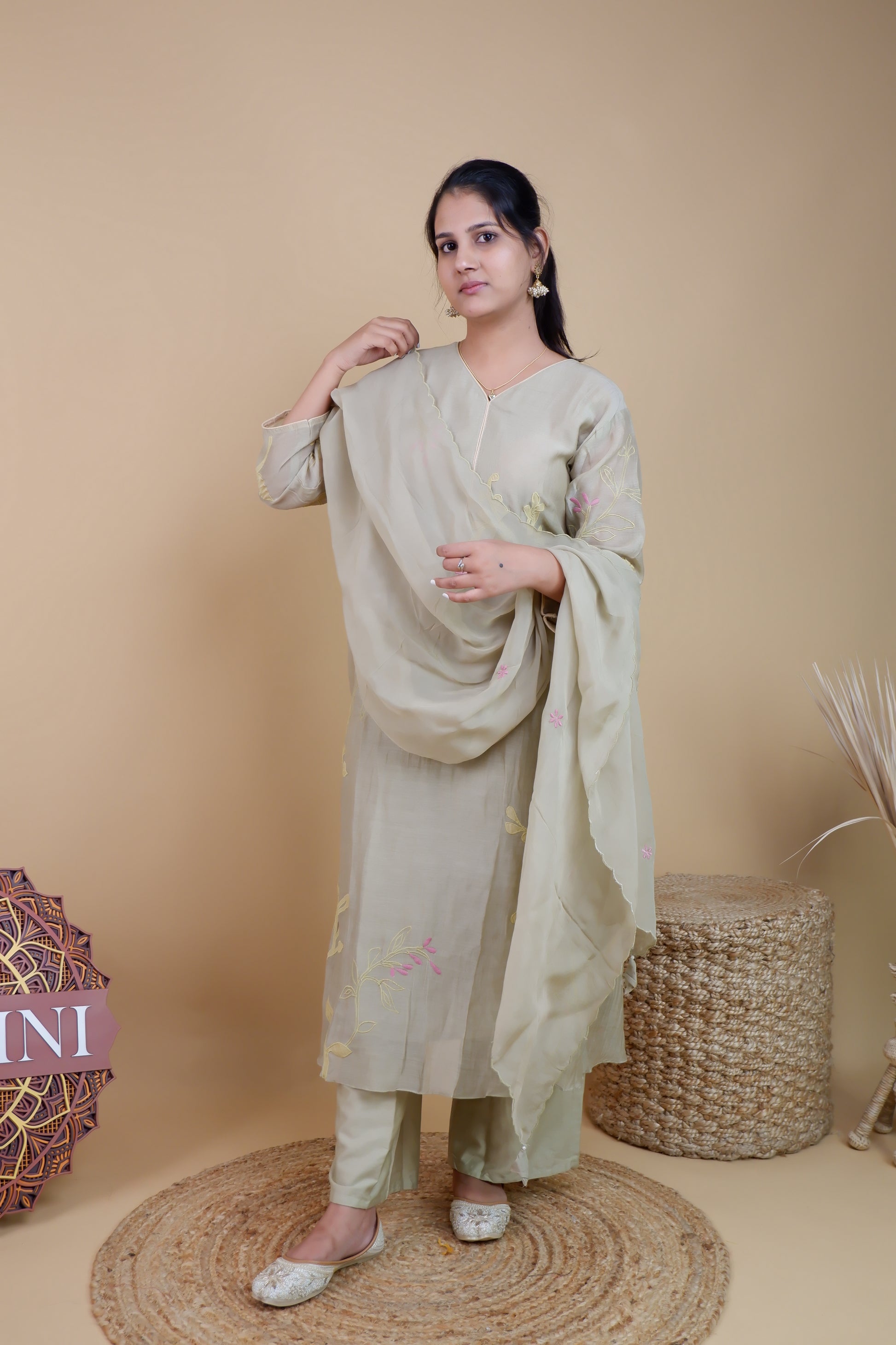 Woman wearing olive chanderi embroidered suit with matching dupatta and pants standing against beige background