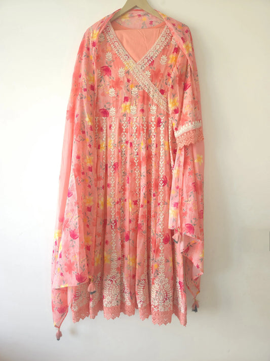 Pink thread work Anarkali suit with floral design and intricate lace details hanging on a wooden hanger