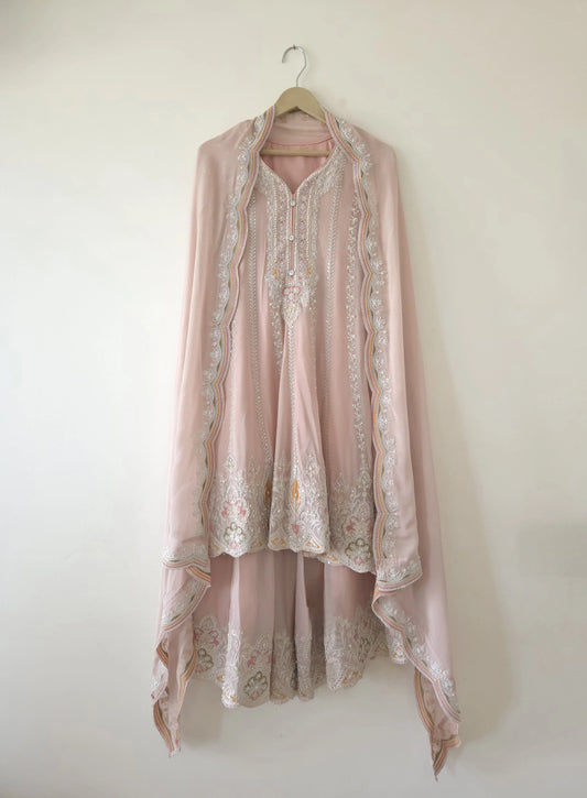 Light pink pure chinon anarkali suit with intricate white and gold embroidery hanging on a wooden hanger