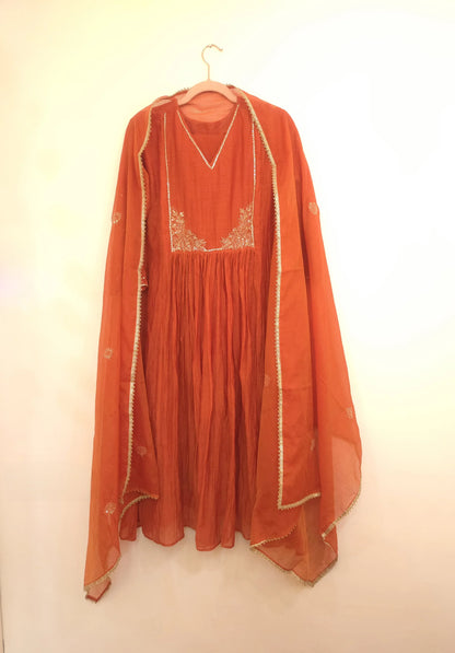 Rust orange Chanderi suit with embroidered neckline and matching dupatta hanging on a hanger