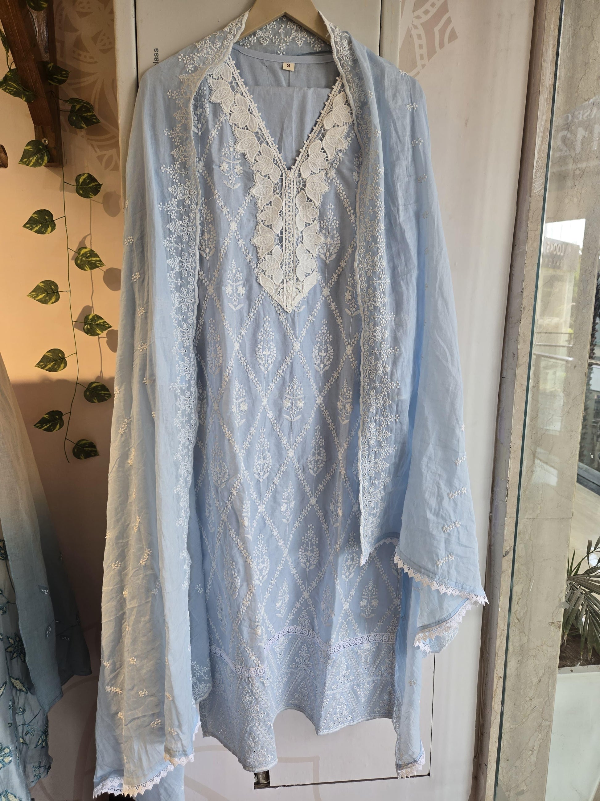 Light blue Schiffli work straight-cut suit with white lace detailing hanging on wooden hanger