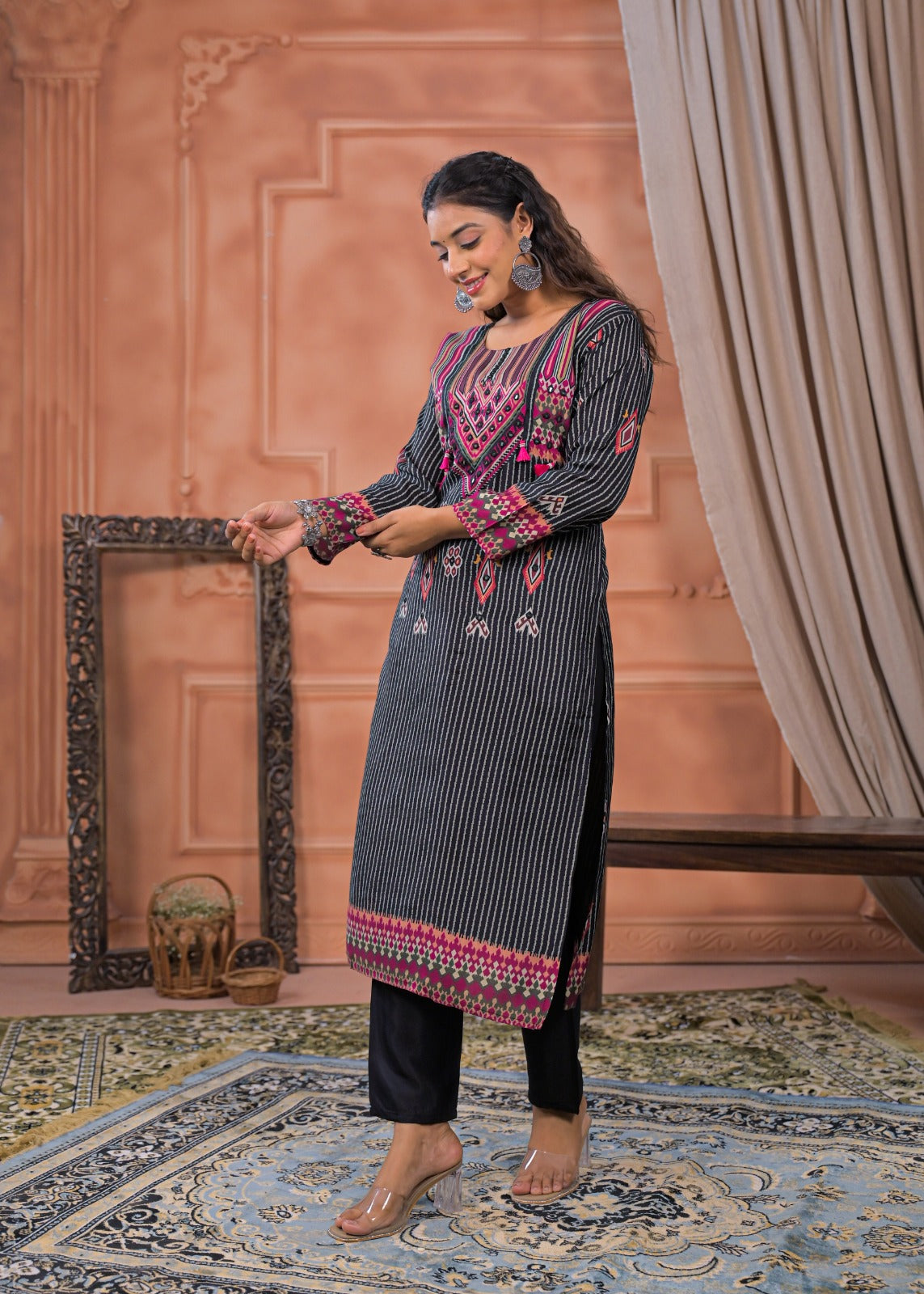 Woman wearing black striped embroidered suit set with pink detailing standing on patterned rug