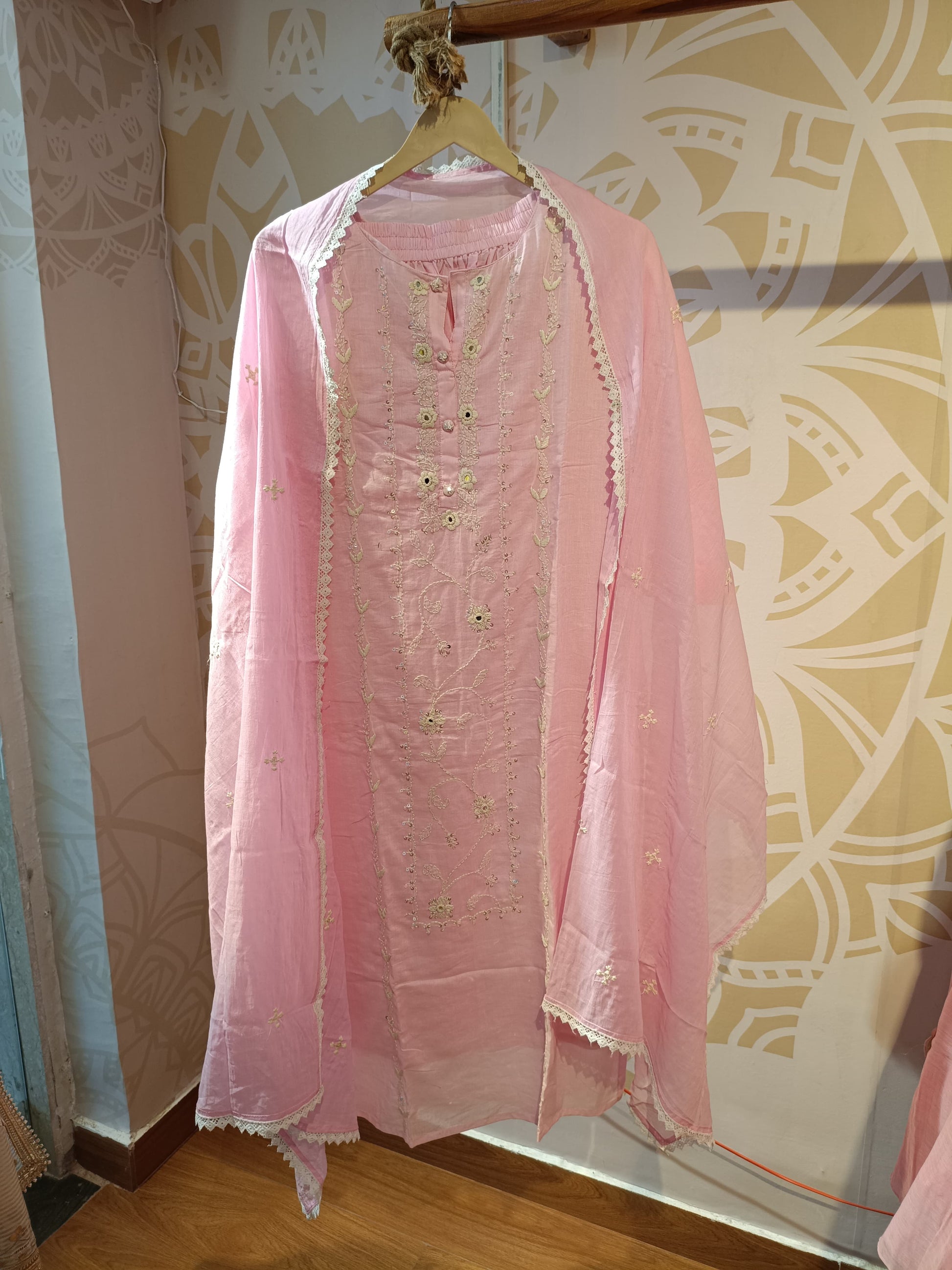 Delicate Indian suit for women in soft pink with intricate embroidery hanging on a wooden hanger