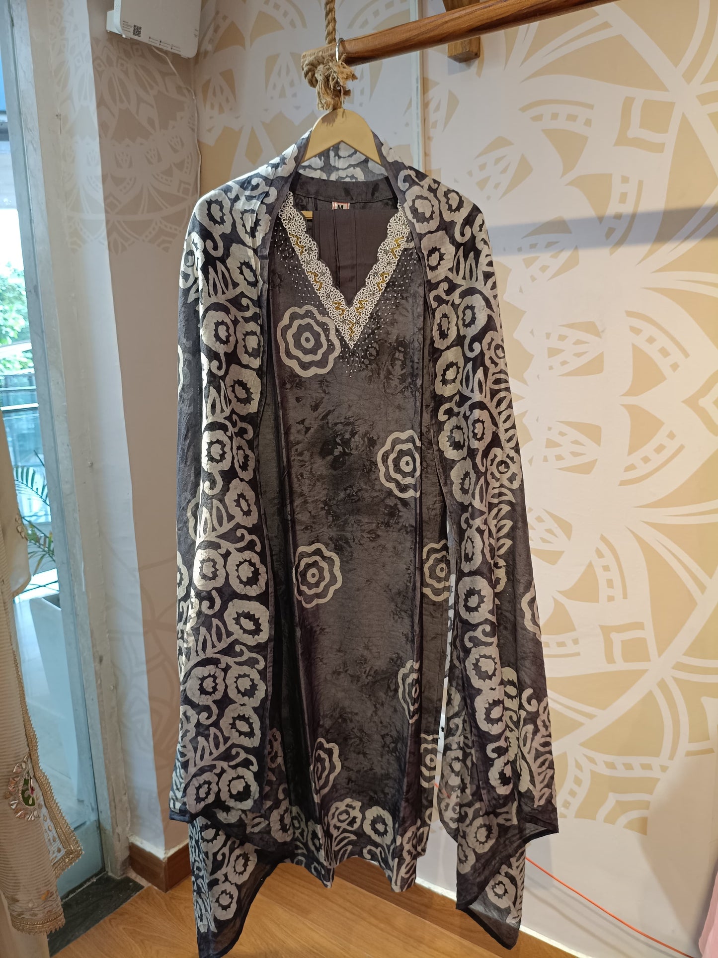Grey and white cotton suit set with floral patterns hanging on a wooden hanger at Dharini's Store
