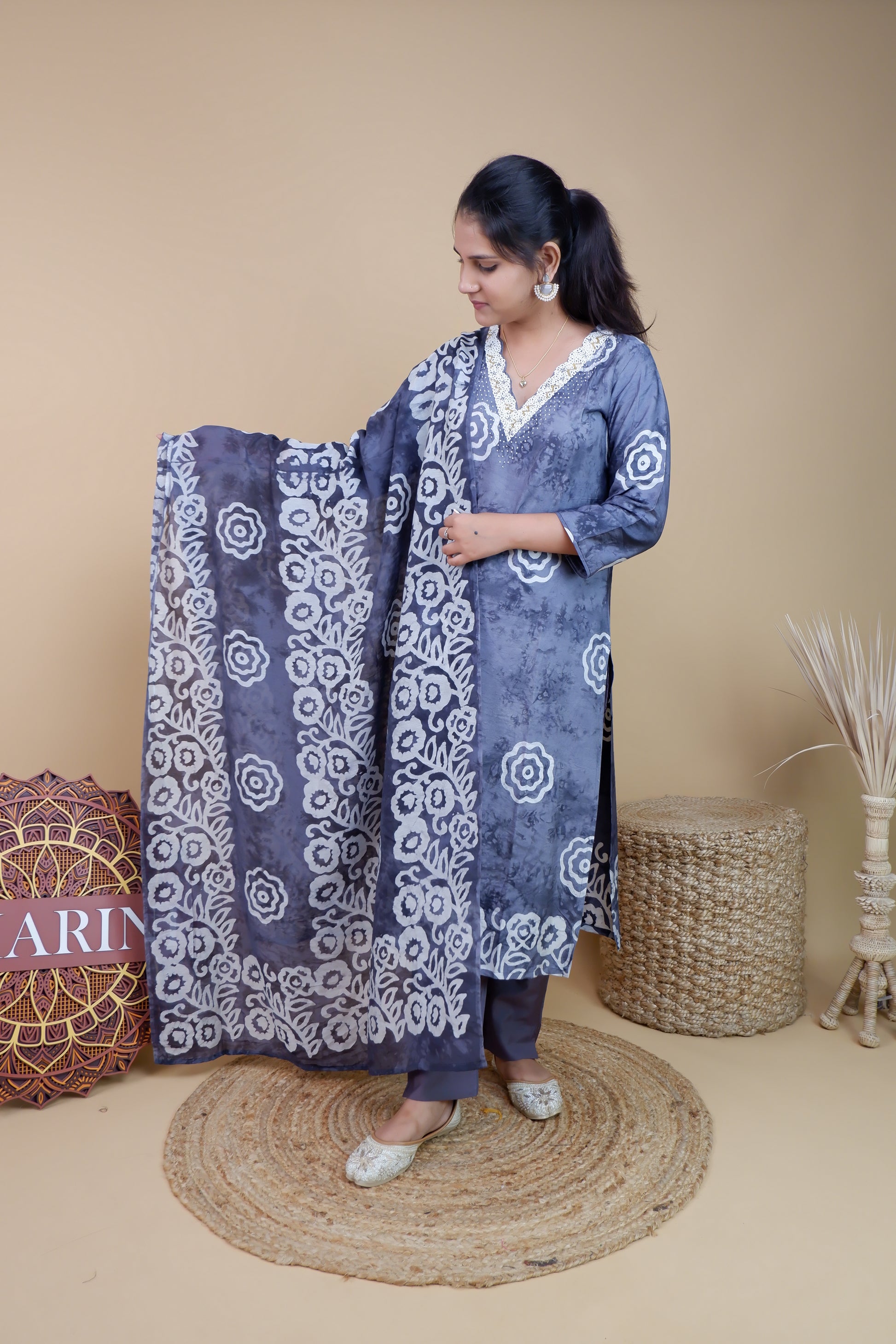Woman wearing grey and white cotton suit set with floral patterns and lace details holding matching dupatta