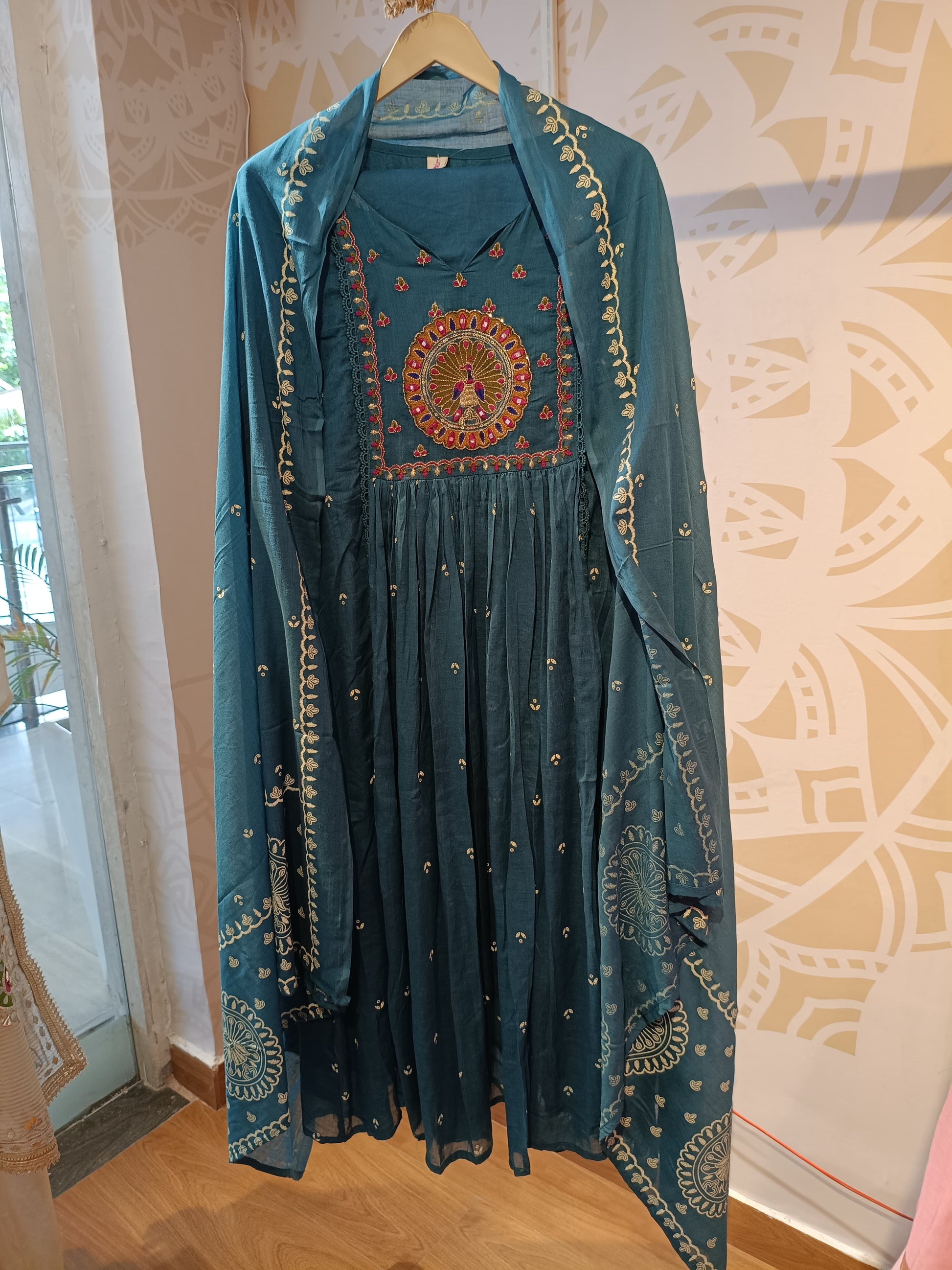Teal cotton anarkali set with intricate embroidery and matching dupatta hanging on wooden hanger