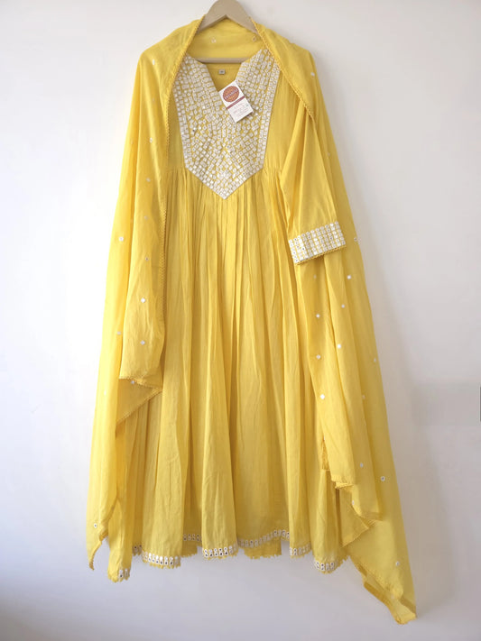 Yellow cotton anarkali dress with white embroidery on neckline and matching dupatta hanging on wall