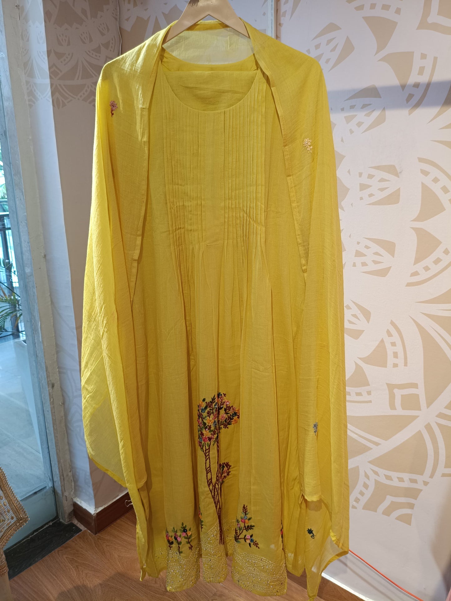 Yellow embroidered cotton dress with floral stitch detailing hanging on a wooden hanger
