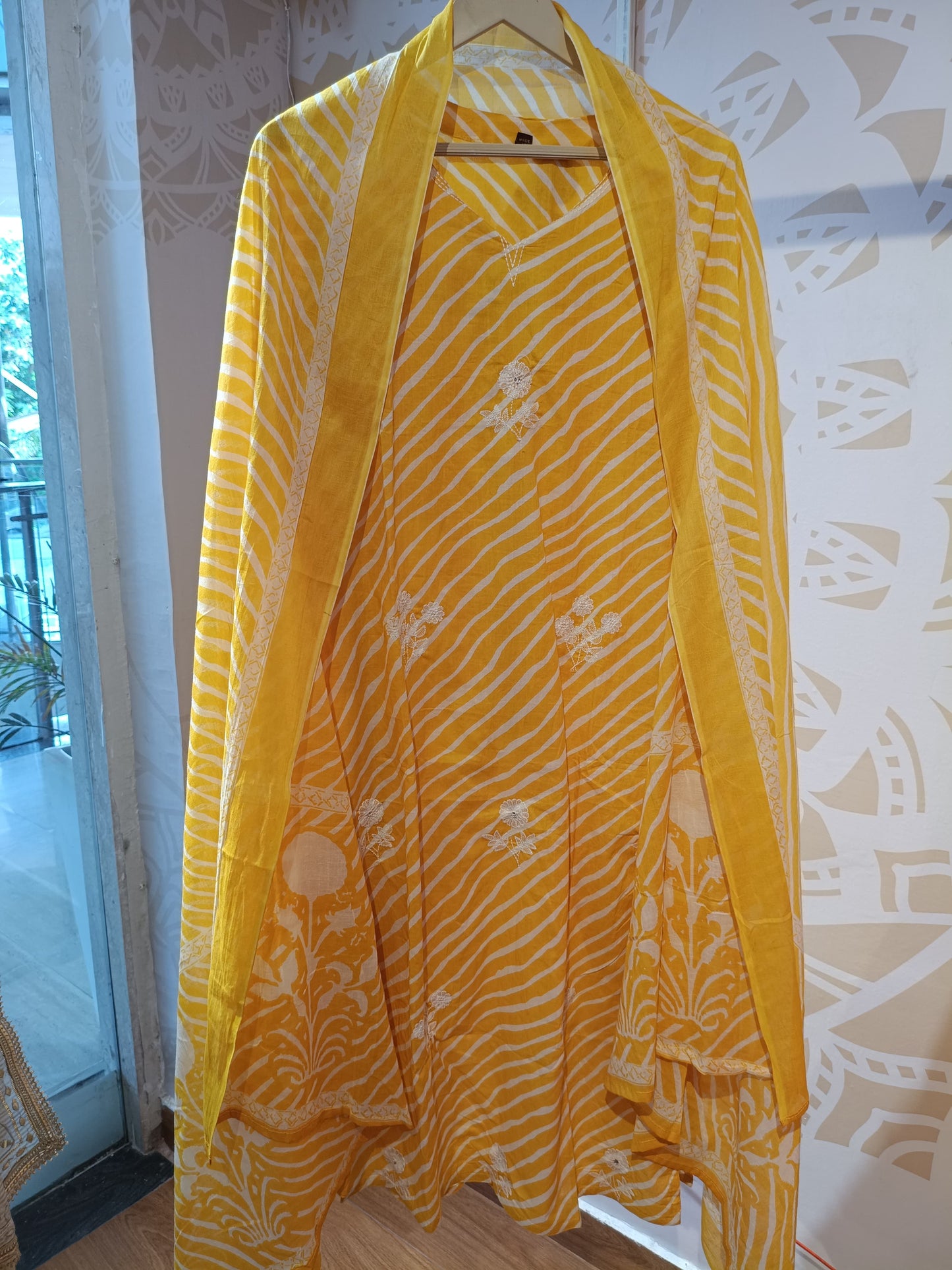 Yellow striped cotton suit with white floral patterns hanging indoors at Dharini's Store