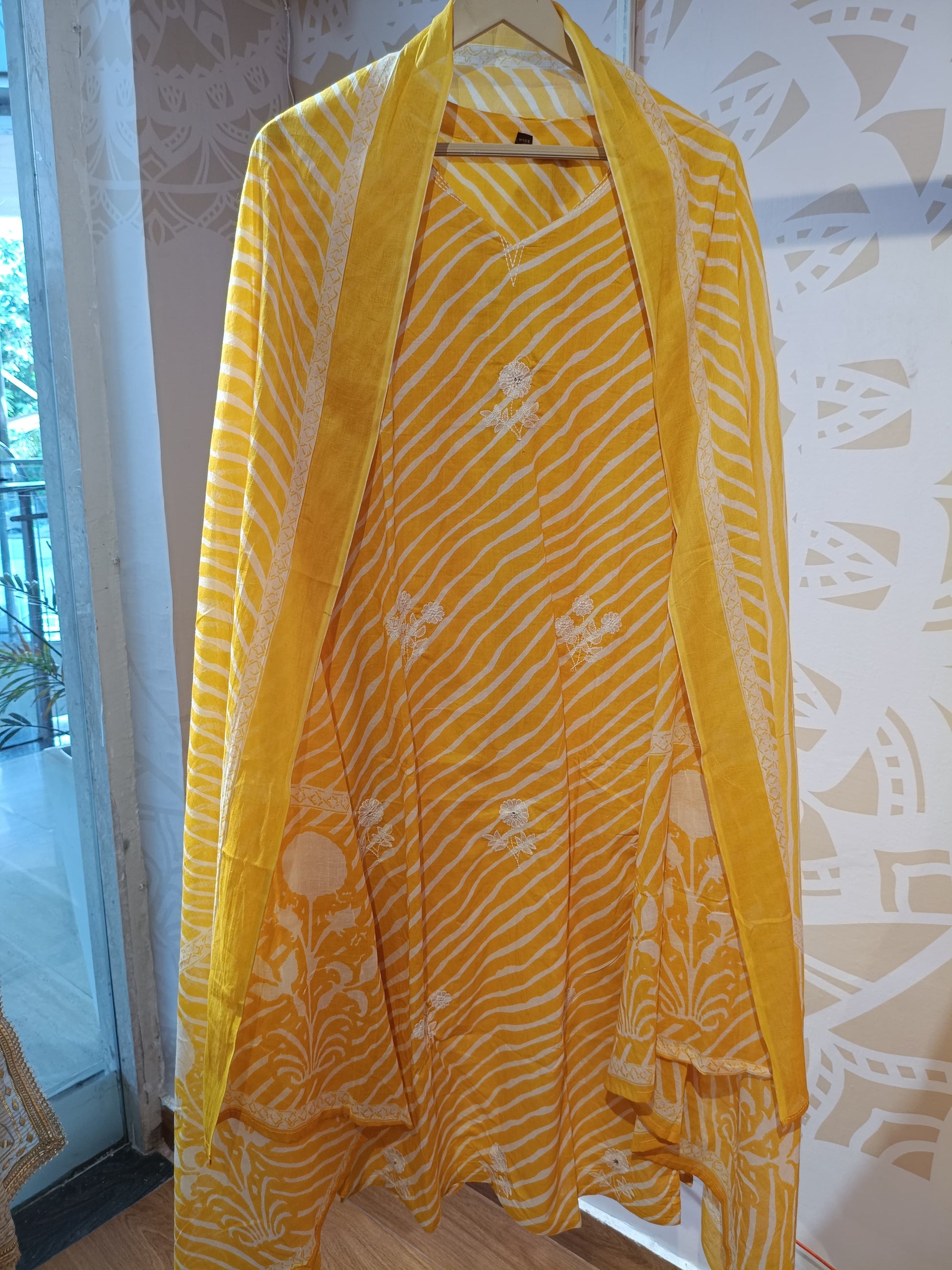 Yellow striped cotton suit with white floral patterns hanging indoors at Dharini's Store