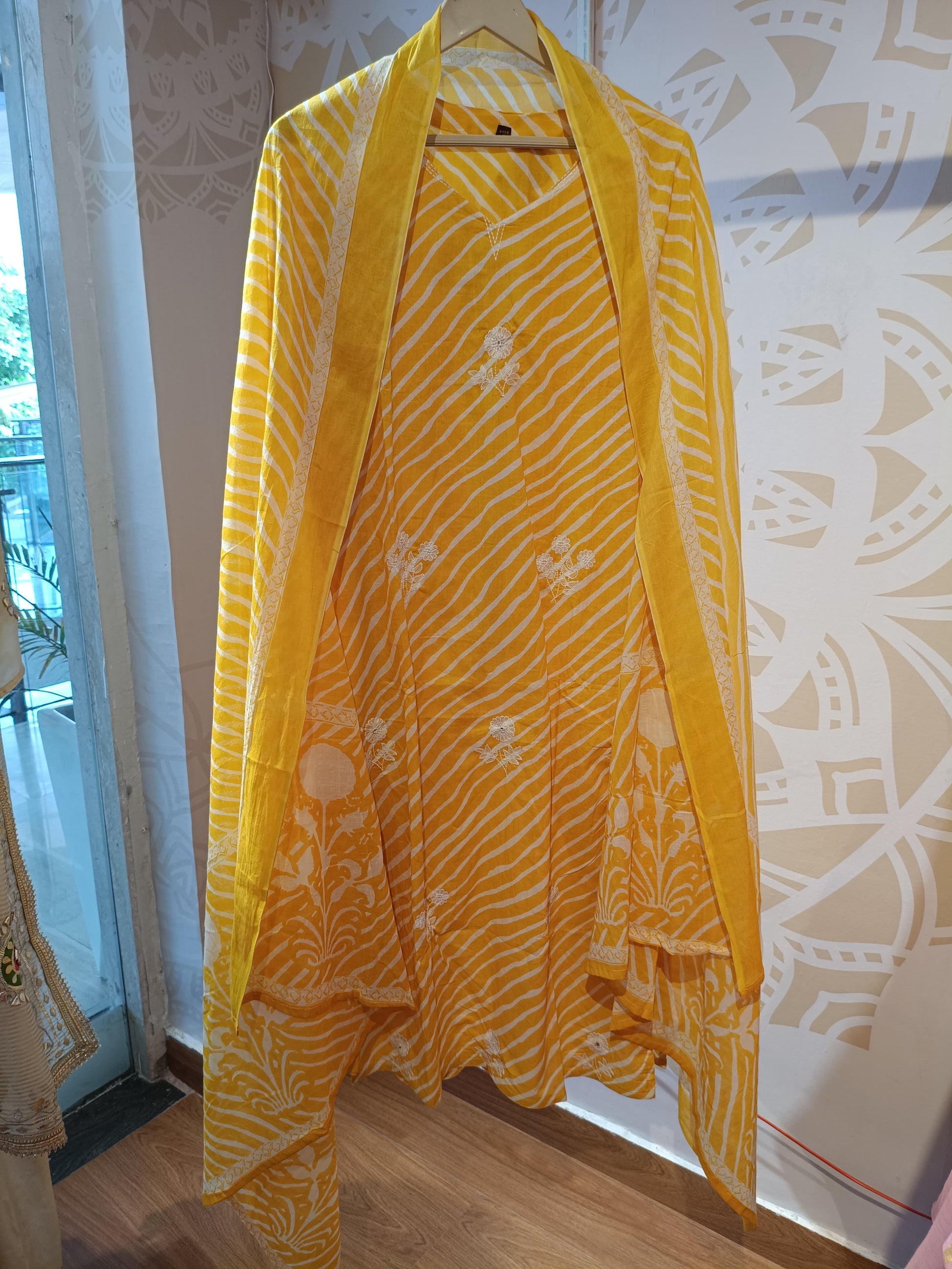 Yellow striped cotton suit with floral patterns hanging on a wooden hanger indoors